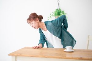 テーブルにつかまり腰を押さえる女性