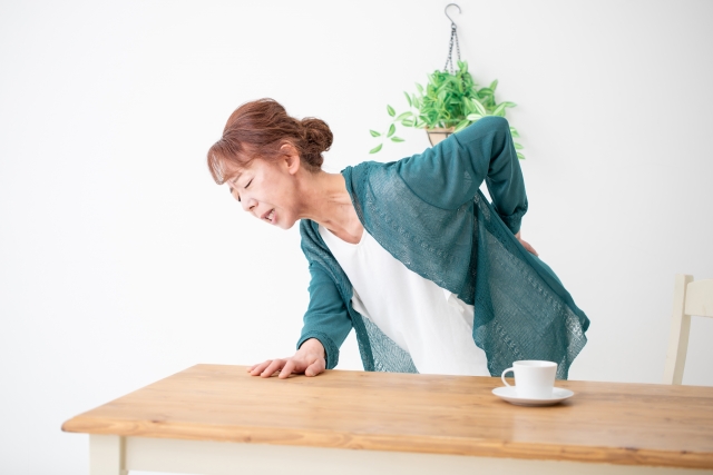 テーブルにつかまり腰を押さえる女性